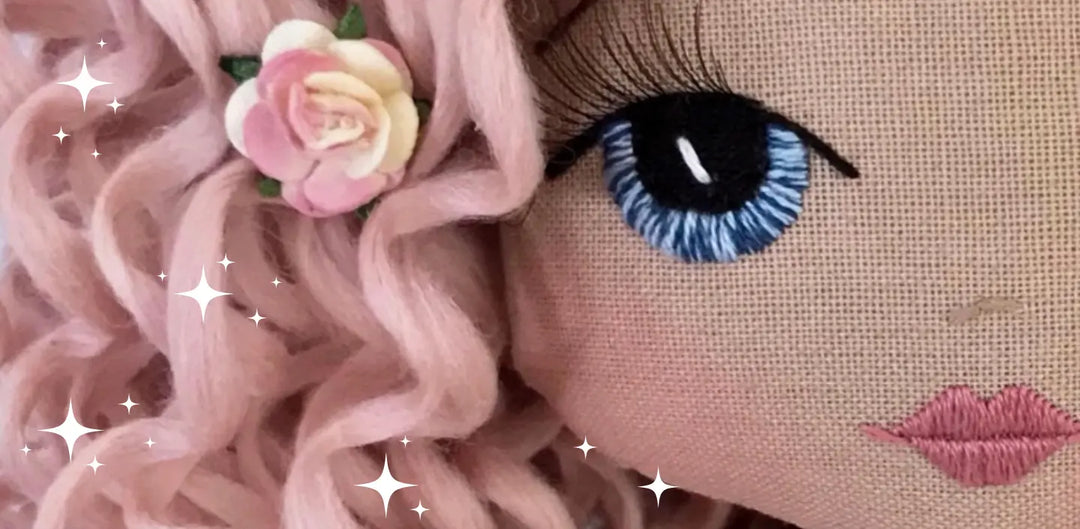 Close up of handmade doll embroidered face with realistic eyelashes and pink curly hair