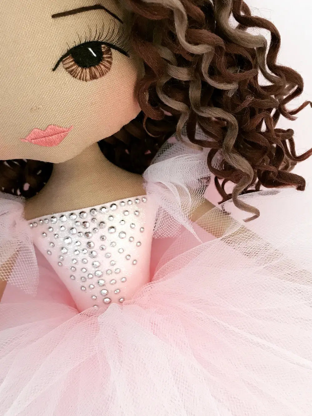 close up detail of ballerina doll showcasing brown eyes, brunette curls and pink tutu with silver diamante detail inspired by tutu du monde dress