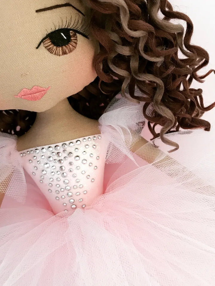 close up detail of ballerina doll showcasing brown eyes, brunette curls and pink tutu with silver diamante detail inspired by tutu du monde dress