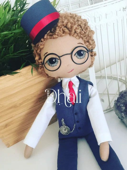 boy train conductor doll wearing a blue and red hat, glasses, red neck tie, white shirt and blue train conductor suit with clock watch