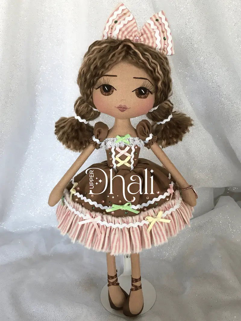 Gingerbread Girl Christmas Ornamental doll wearing a fun gingerbread brown dress with white and pink stripe ruffles, pink, green and yellow ribbon detail, diamante sparkle and brown hair with ricrac ribbon detail