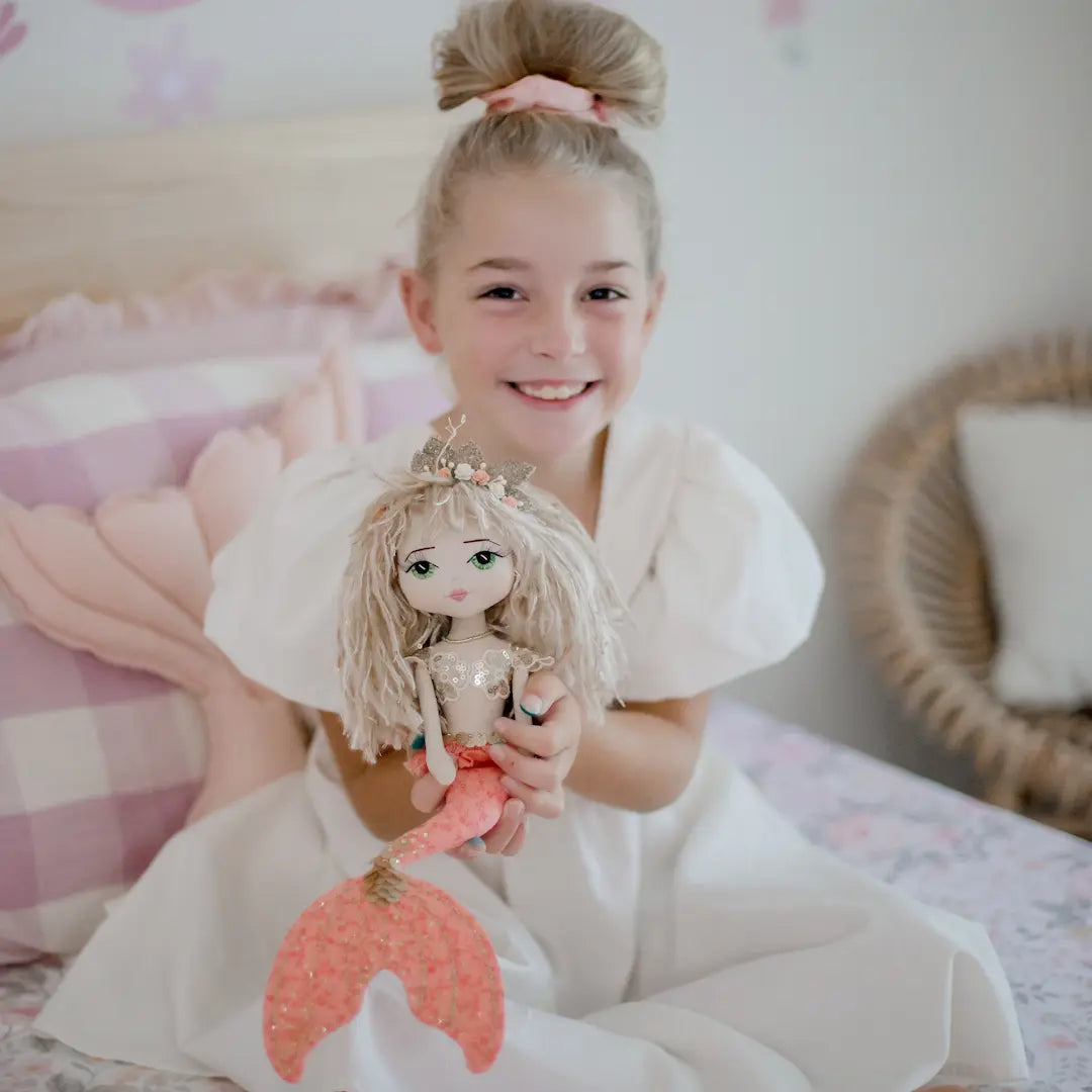 Coral mermaid with gold sequin top held by a young girl in her mermaid themed bedroom