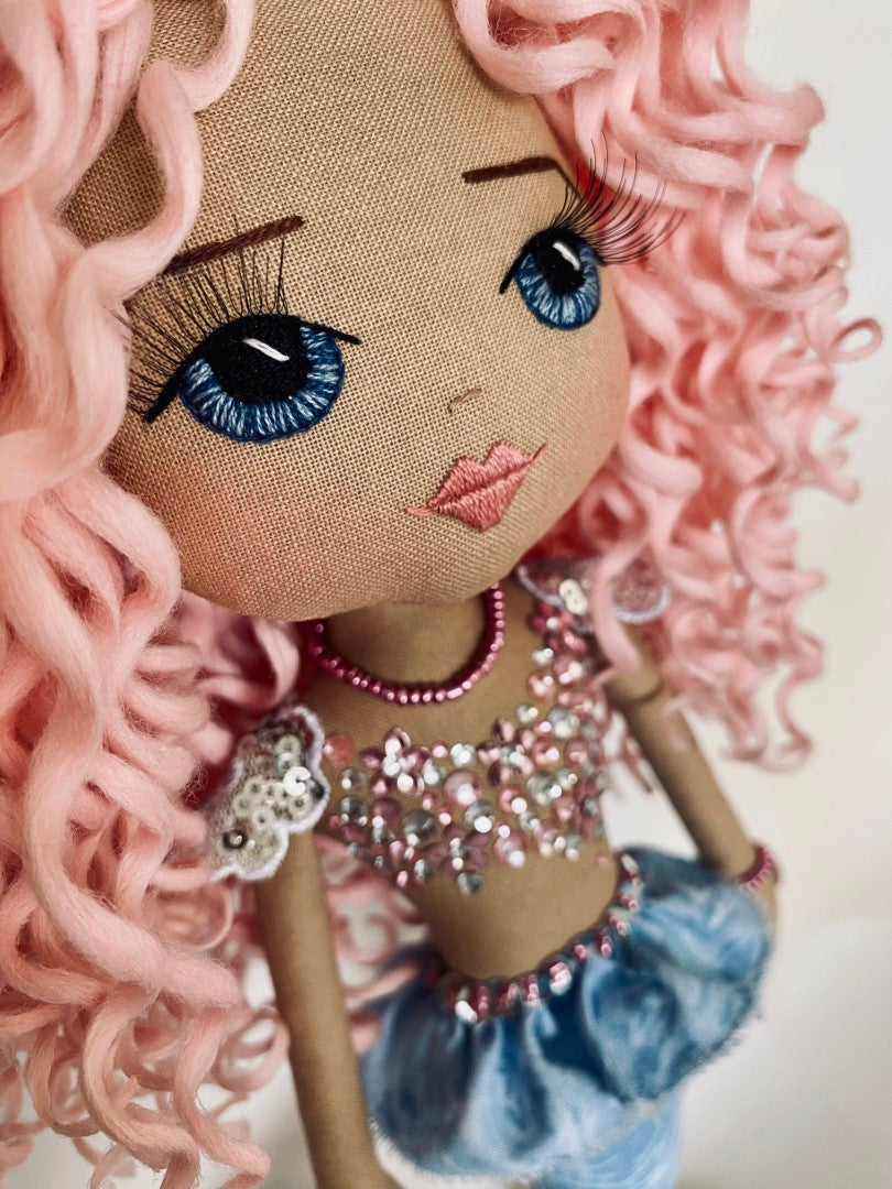 Mermaid Doll with blue tail, pink and silver diamante detail and mermaid bra. Curly hair made from hand rolled pink mohair fibre and a mermaid crown in silver with blue sequin detail. Doll features a hand embroidered face featuring blue eyes, pink lips and three dimensional eye lashes.