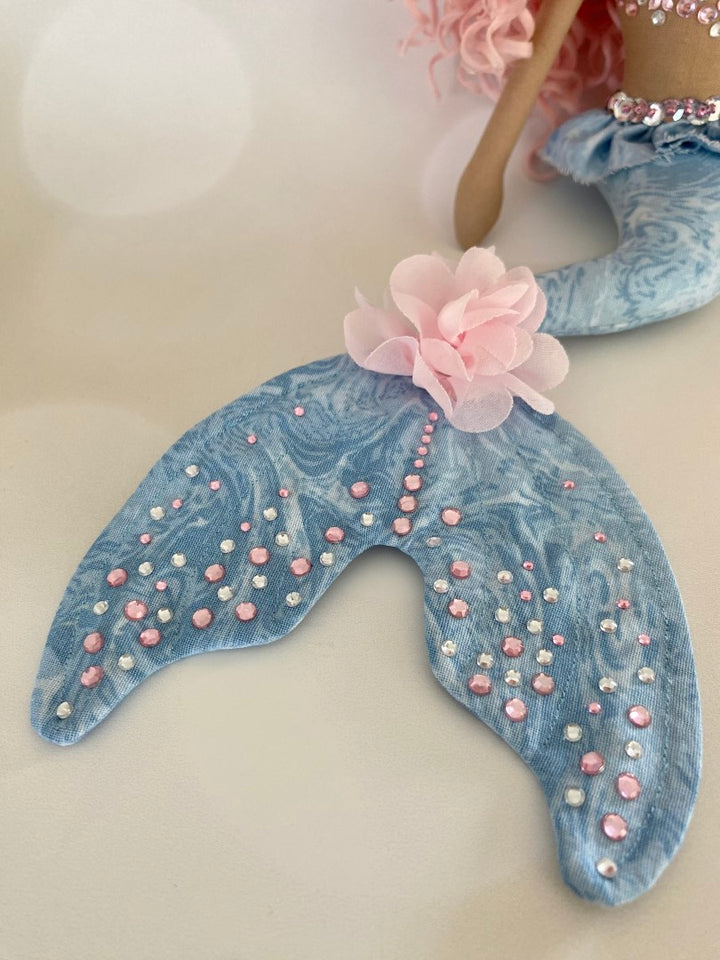 Mermaid Doll with blue tail, pink and silver diamante detail and mermaid bra. Curly hair made from hand rolled pink mohair fibre and a mermaid crown in silver with blue sequin detail. Doll features a hand embroidered face featuring blue eyes, pink lips and three dimensional eye lashes.