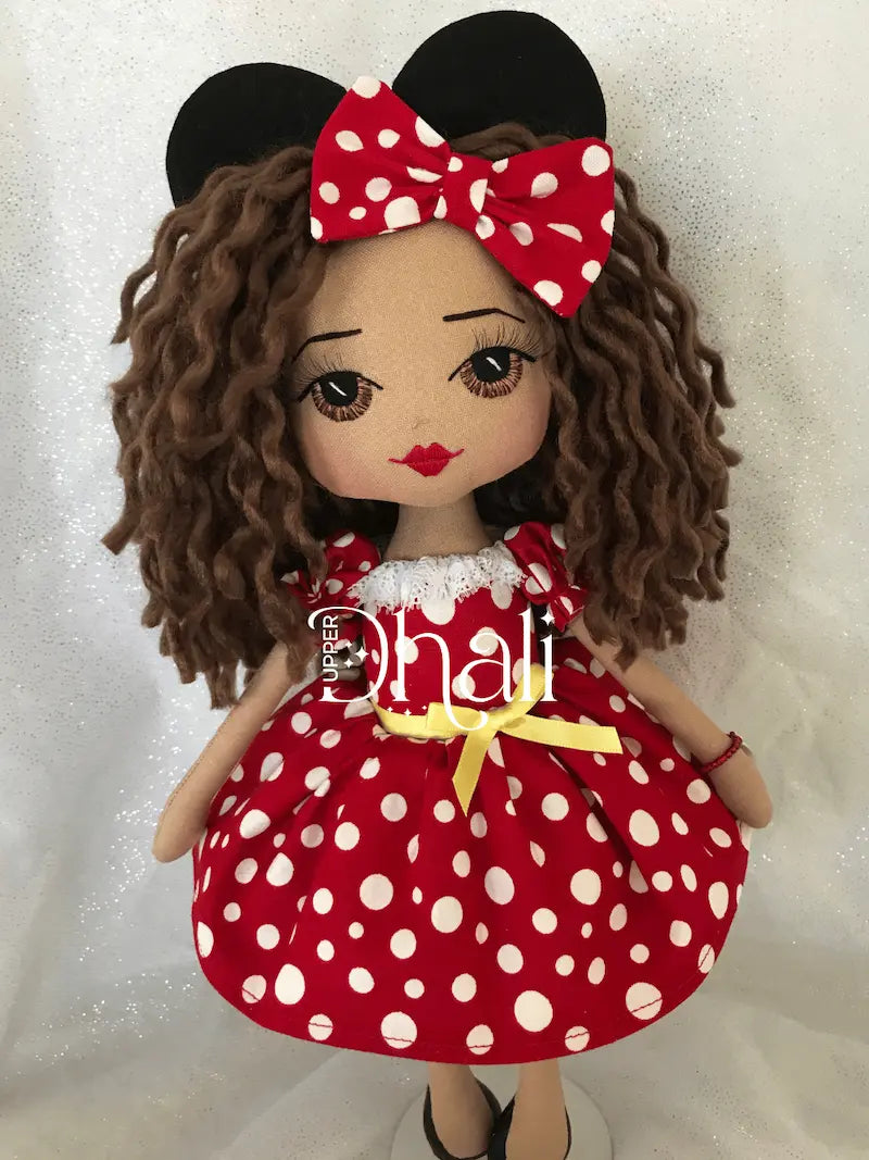 Minnie Fan Girl handmade doll featuring a red dress with white spots, yellow ribbon waist detail, long brown hair, hand embroidered brown eye and black mouse hair accessory