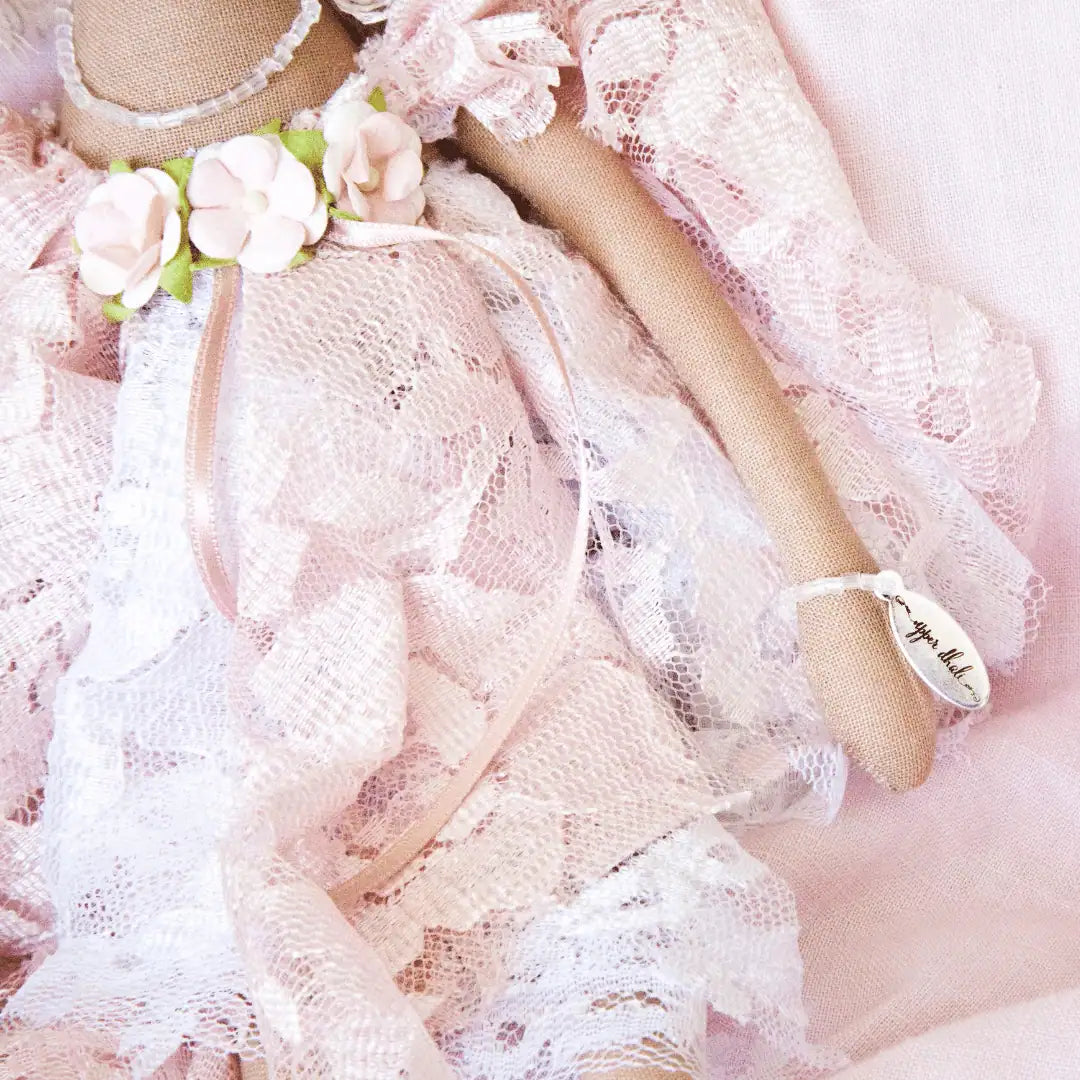 handmade doll wearing a  pink and white lace vintage inspired dress with flower bodice detail, showcasing the authenticity bracelet with Upper Dhali engraved charm