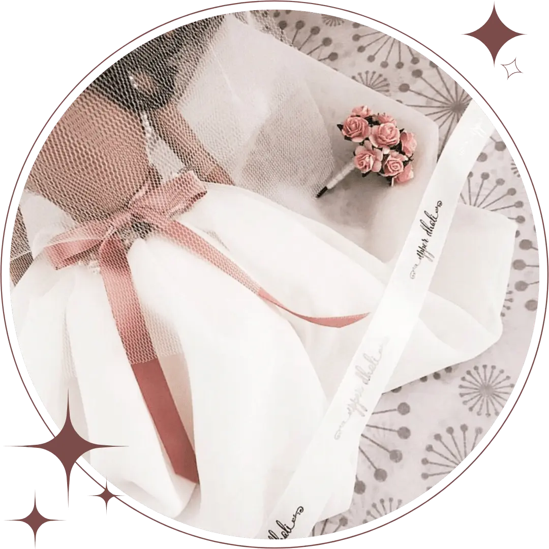wedding dress keepsake doll wearing a white wedding dress, pink sash, miniature pink rose bouquet; draped in an Upper Dhali branded white ribbon