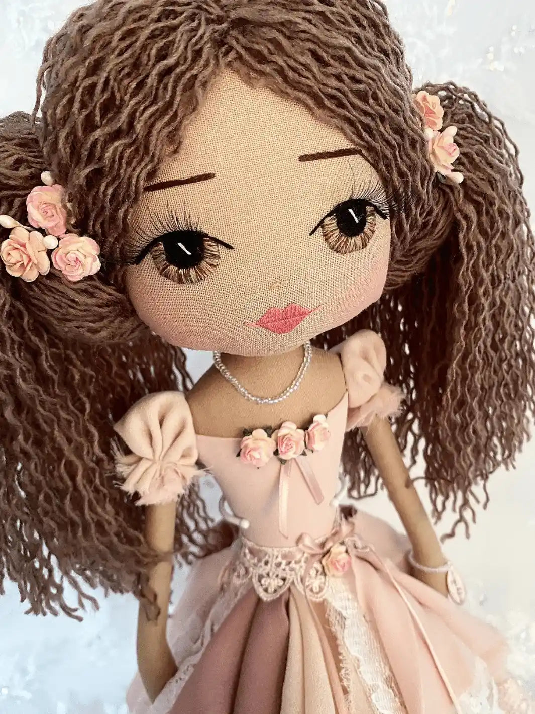 handmade doll with hand embroidered brown eyes, long brown hair in ponytails with flower detail, wearing a vintage inspired chiffon and lace dress in pink tones with flower and ribbon detail