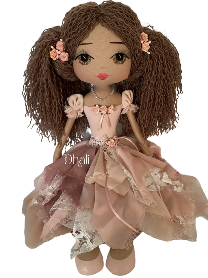 handmade doll with hand embroidered brown eyes, long brown hair in ponytails with flower detail, wearing a vintage inspired chiffon and lace dress in pink tones with flower and ribbon detail