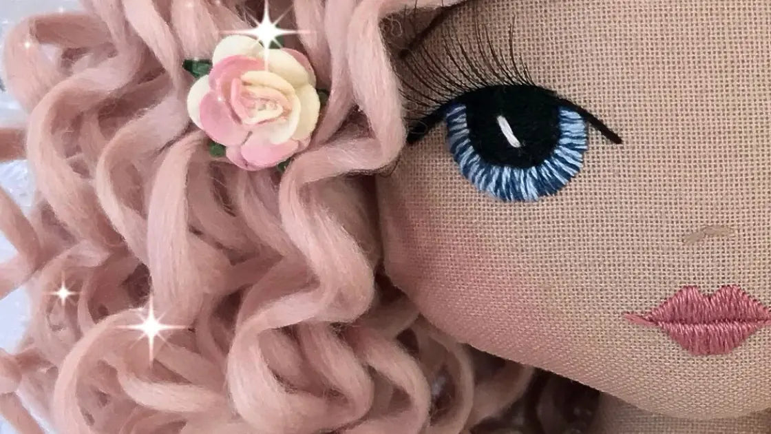 close up of hand embroidered doll face with blue eyes and pink curly hair