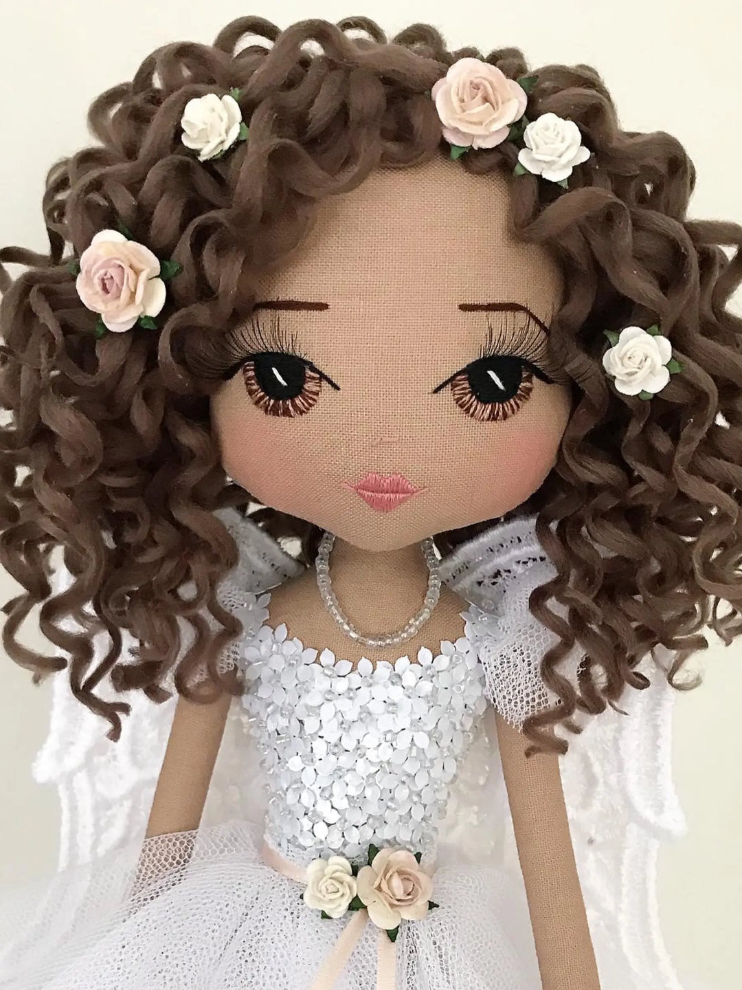 Doll with curly hair adorned with flowers, wearing a white dress and necklace.