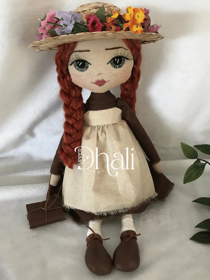 Anne Shirley Green Gables handmade doll featuring a plain brown dress, calico apron dress, long red plaits, hand embroidered face with blue eyes and a straw hat with flower detail