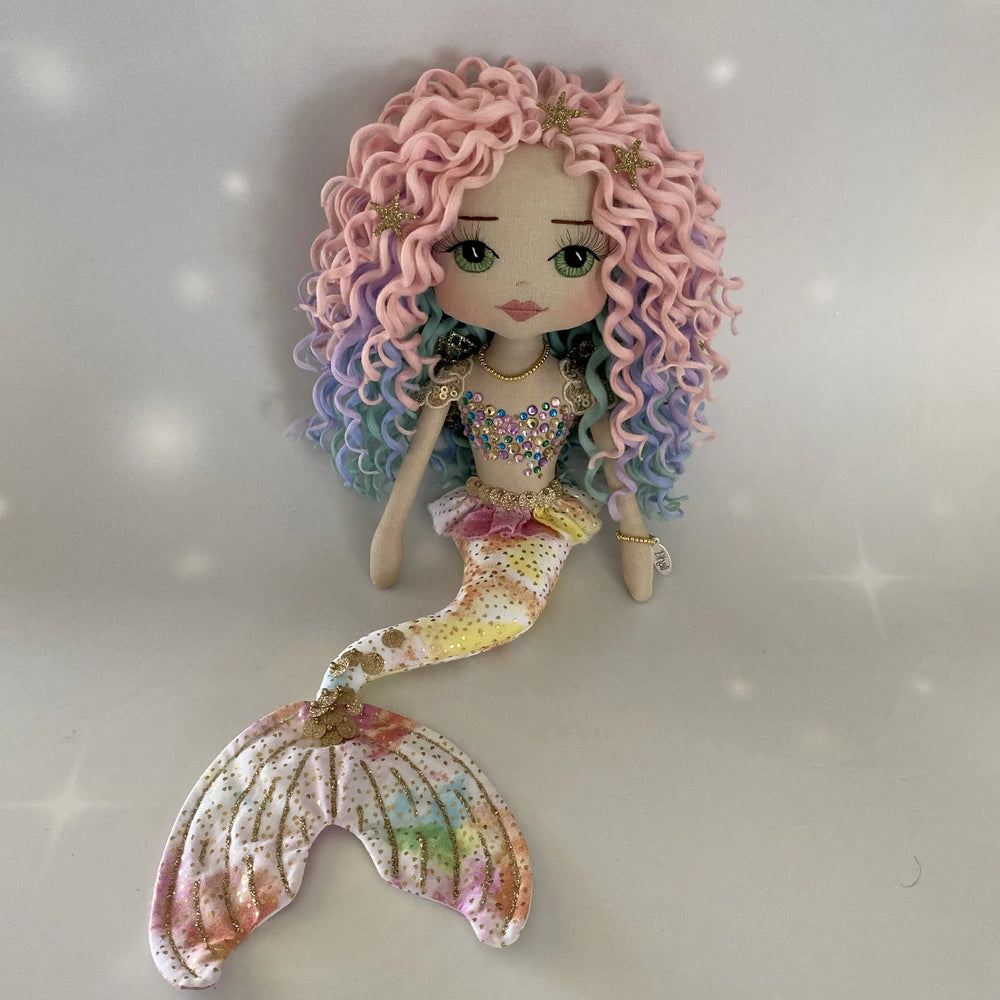 Full-length photo of the Kalani Auralis rainbow mermaid art doll by Upper Dhali, showing her pastel tail, multicolour curls and embellished bodice.