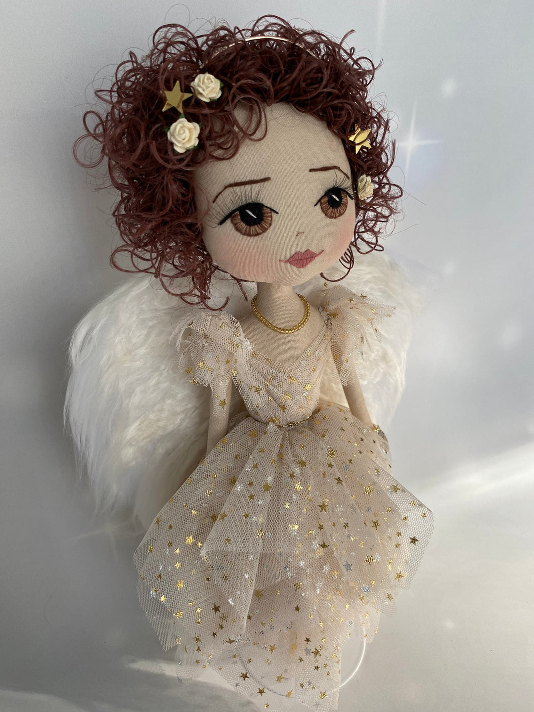 Side view of Christmas angel keepsake featuring brown hand embroidered eyes, brown curly hair, eri silk angel wings and a gold star beige tulle angel gown.