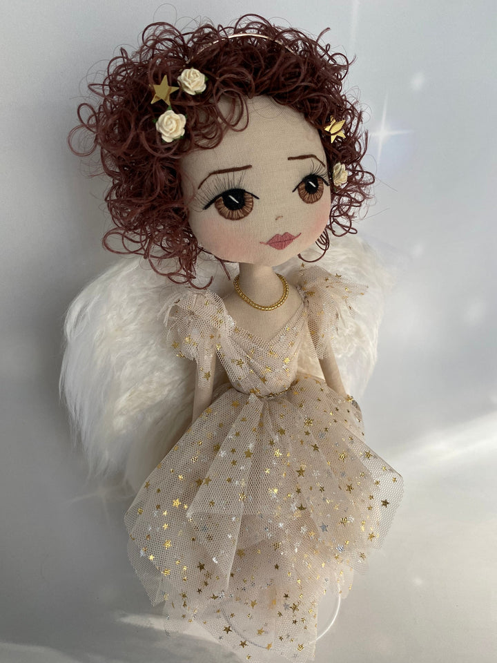 Side view of Christmas angel keepsake featuring brown hand embroidered eyes, brown curly hair, eri silk angel wings and a gold star beige tulle angel gown.