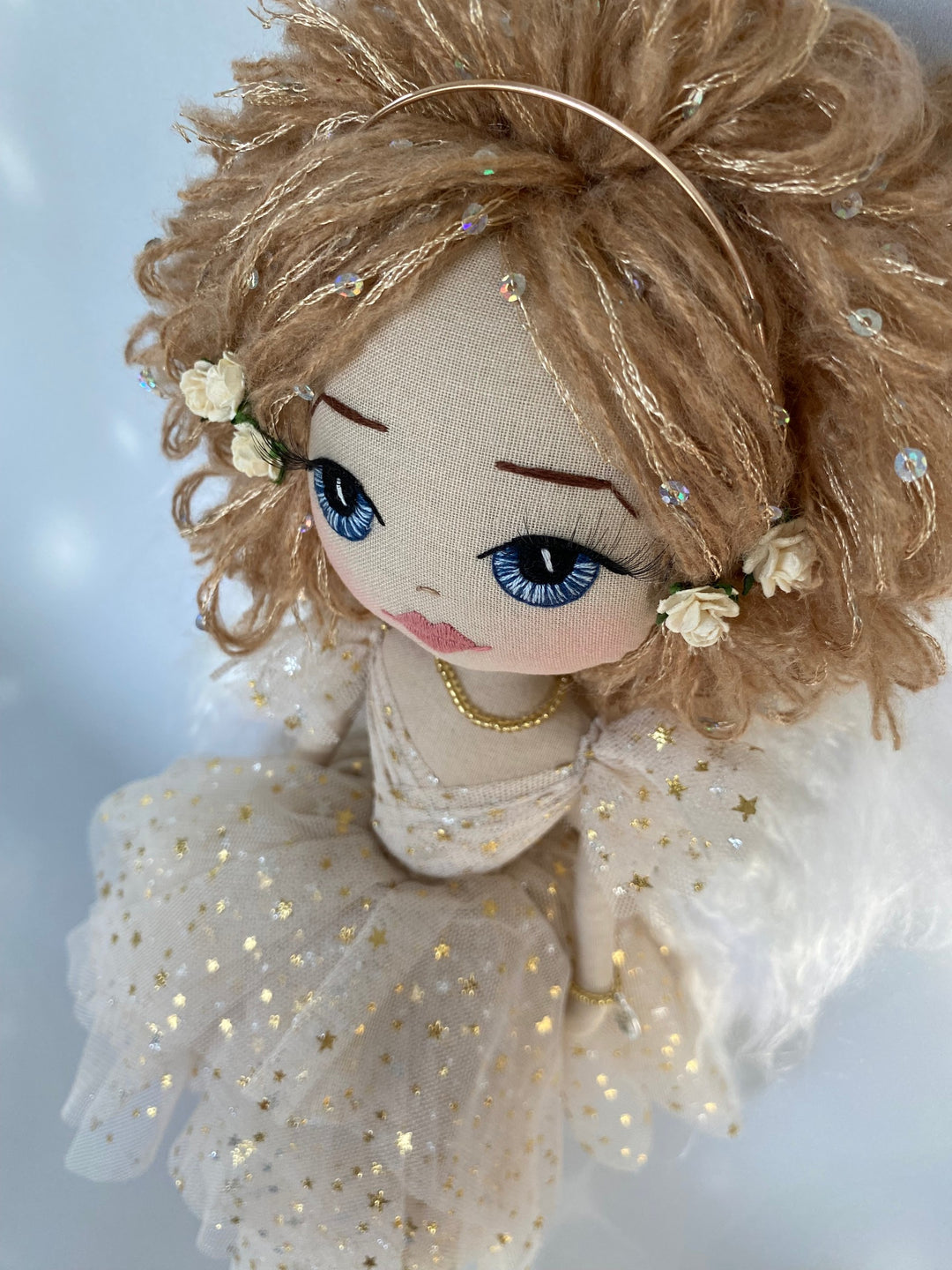 close up view of hand embroidered angel doll face featuring blue eyes and strawberry blond hair