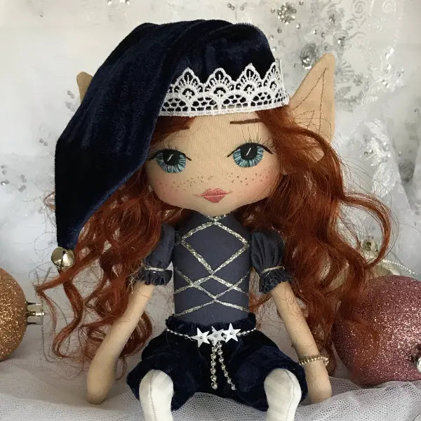 Textile doll with red hair and blue eyes wearing a dark outfit and hat on a decorative background.