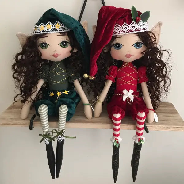 Two dolls dressed in green and red outfits with hats, sitting on a wooden surface.