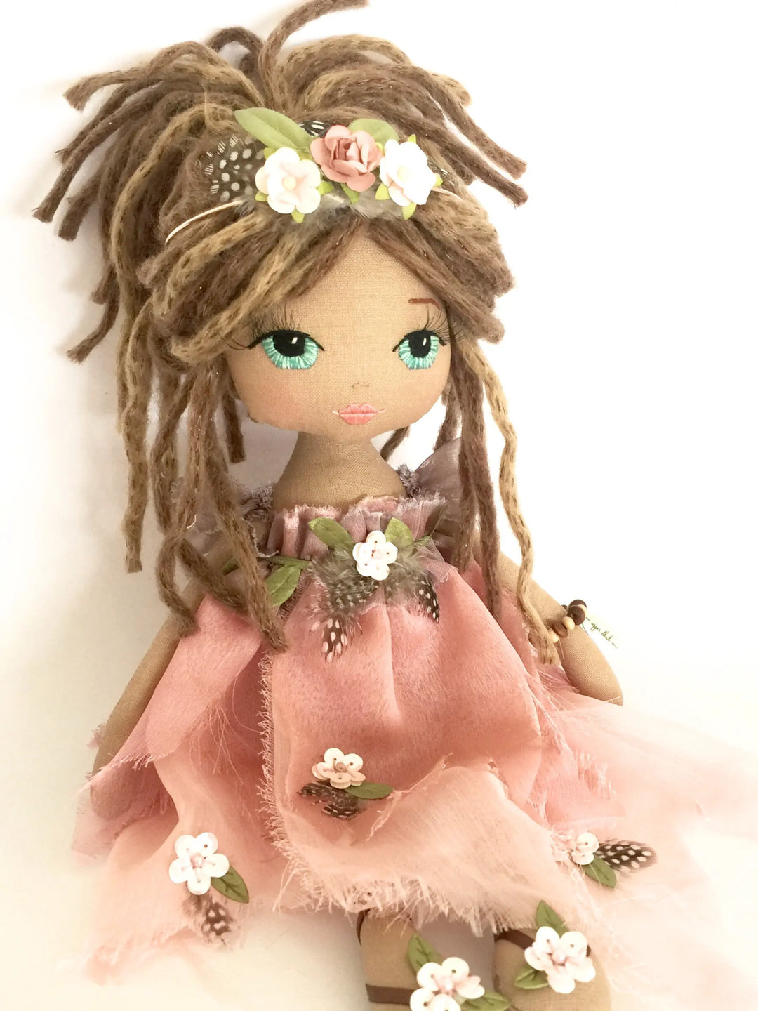 Doll with dreadlocks wearing a pink dress with floral details on a white background