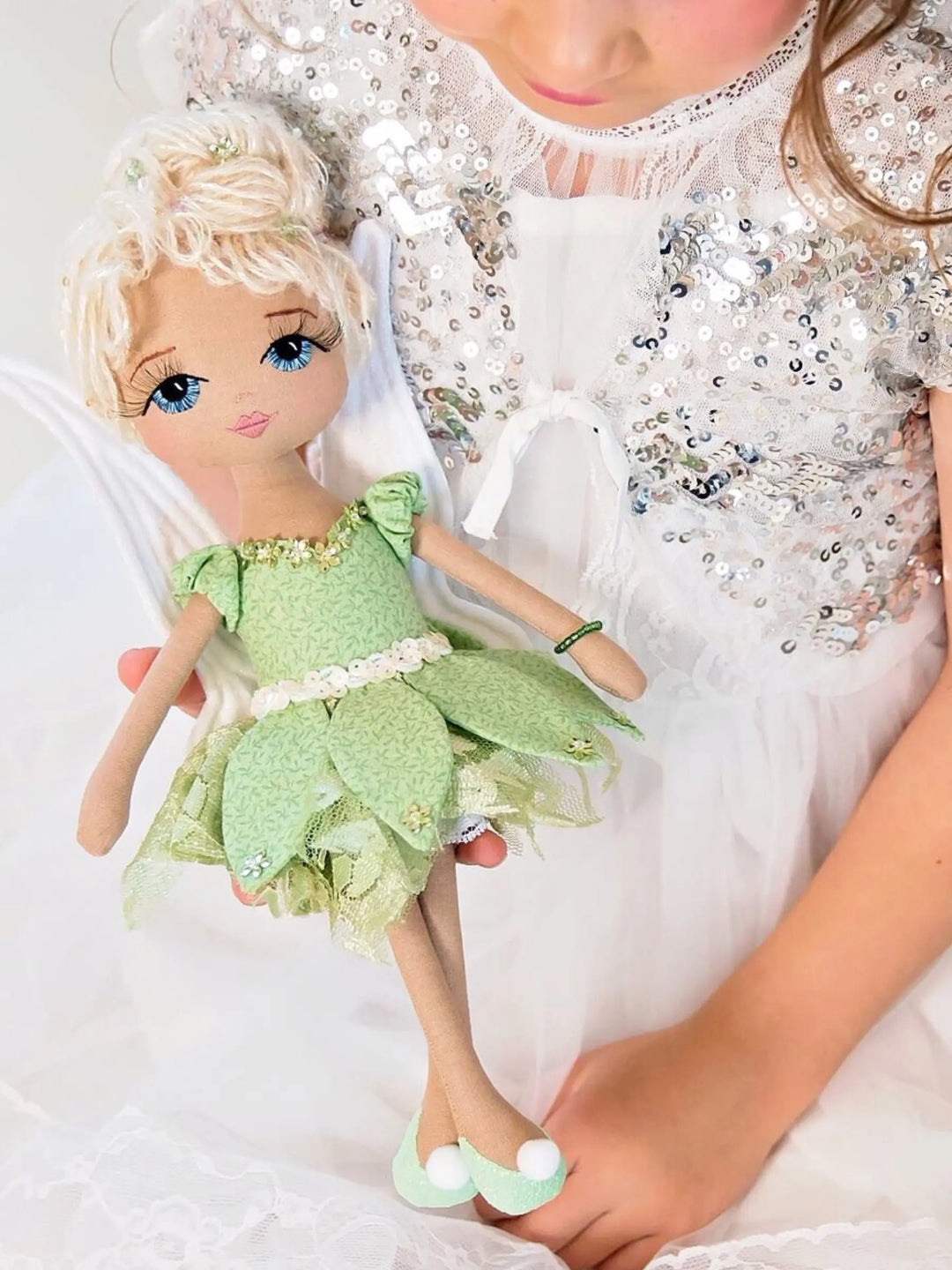 Child holding a fairy doll with a green dress and white wings