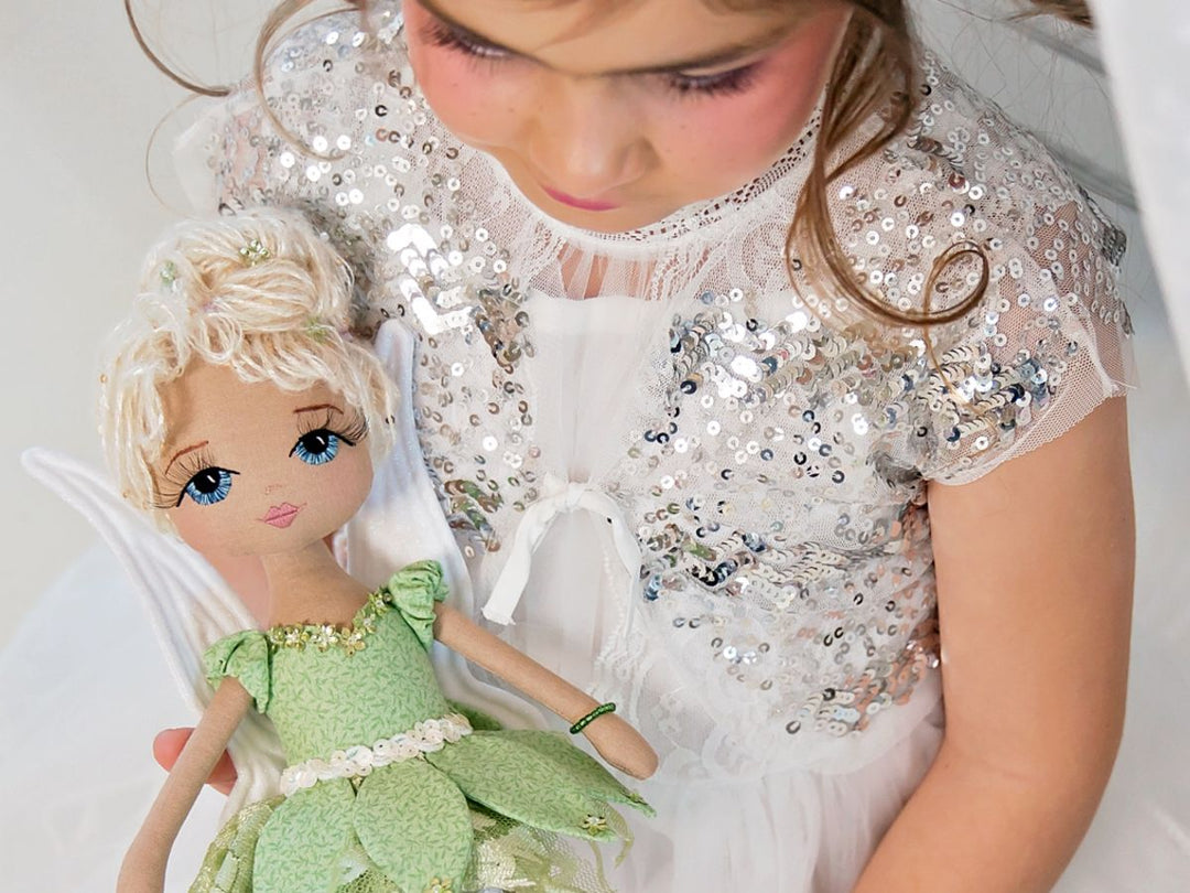 Child in a sequined outfit holding a fairy doll with a green dress.
