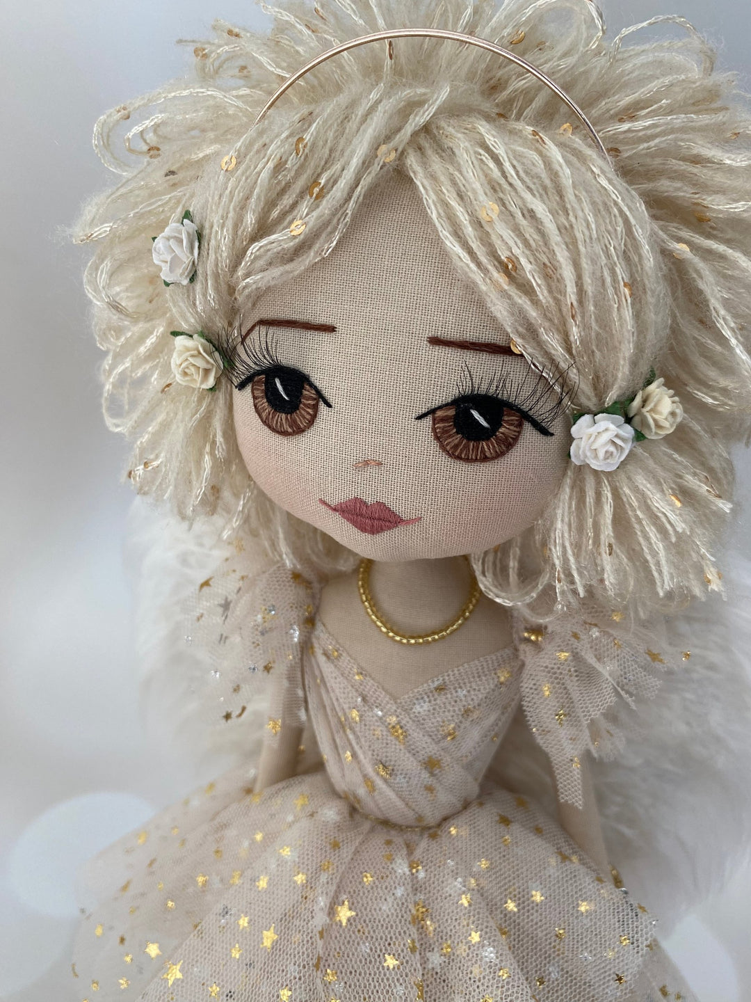 Textile doll with blonde hair, floral accessories, and a gold necklace on a white background