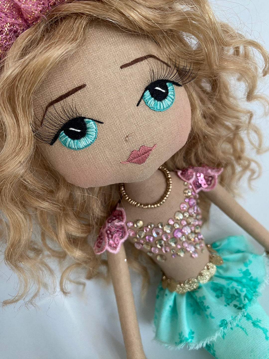 Doll with blonde hair, blue eyes, and a turquoise outfit on a white background