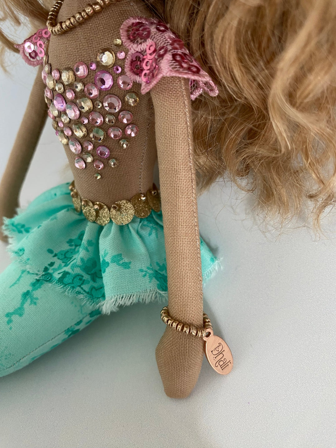 Close-up of a doll with embellished outfit and turquoise skirt on a light background