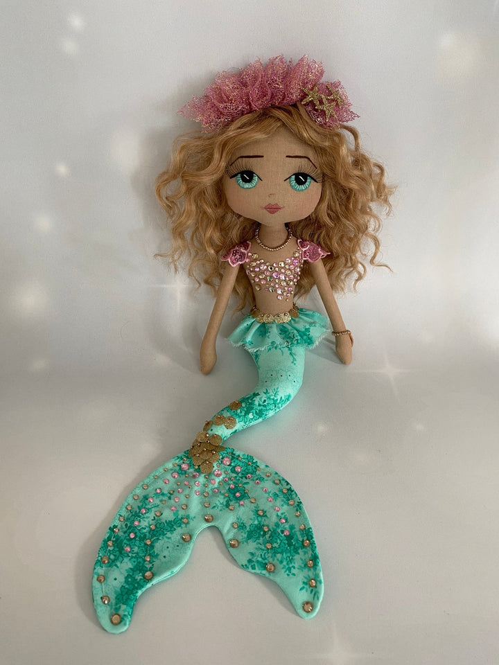 Mermaid doll with a green tail and pink hair accessory on a white background