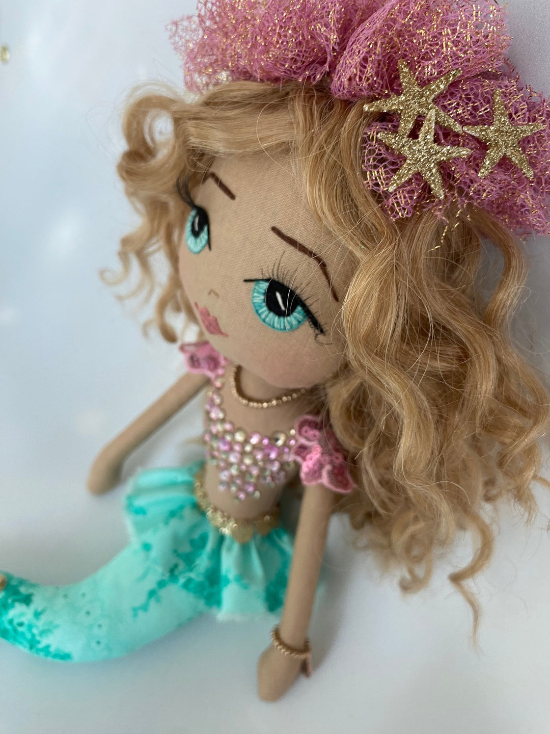 Mermaid doll with blonde hair, blue eyes, and a pink top on a white background