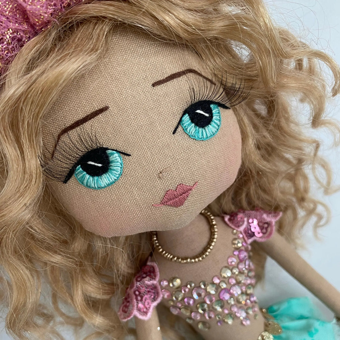 Close-up of a mermaid doll with blonde hair, jade green eyes, and decorative clothing.