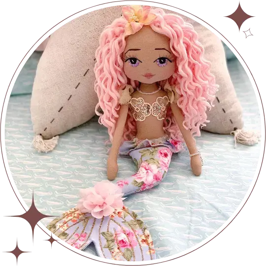 Mermaid doll with pink hair and floral tail sitting on a textured surface.