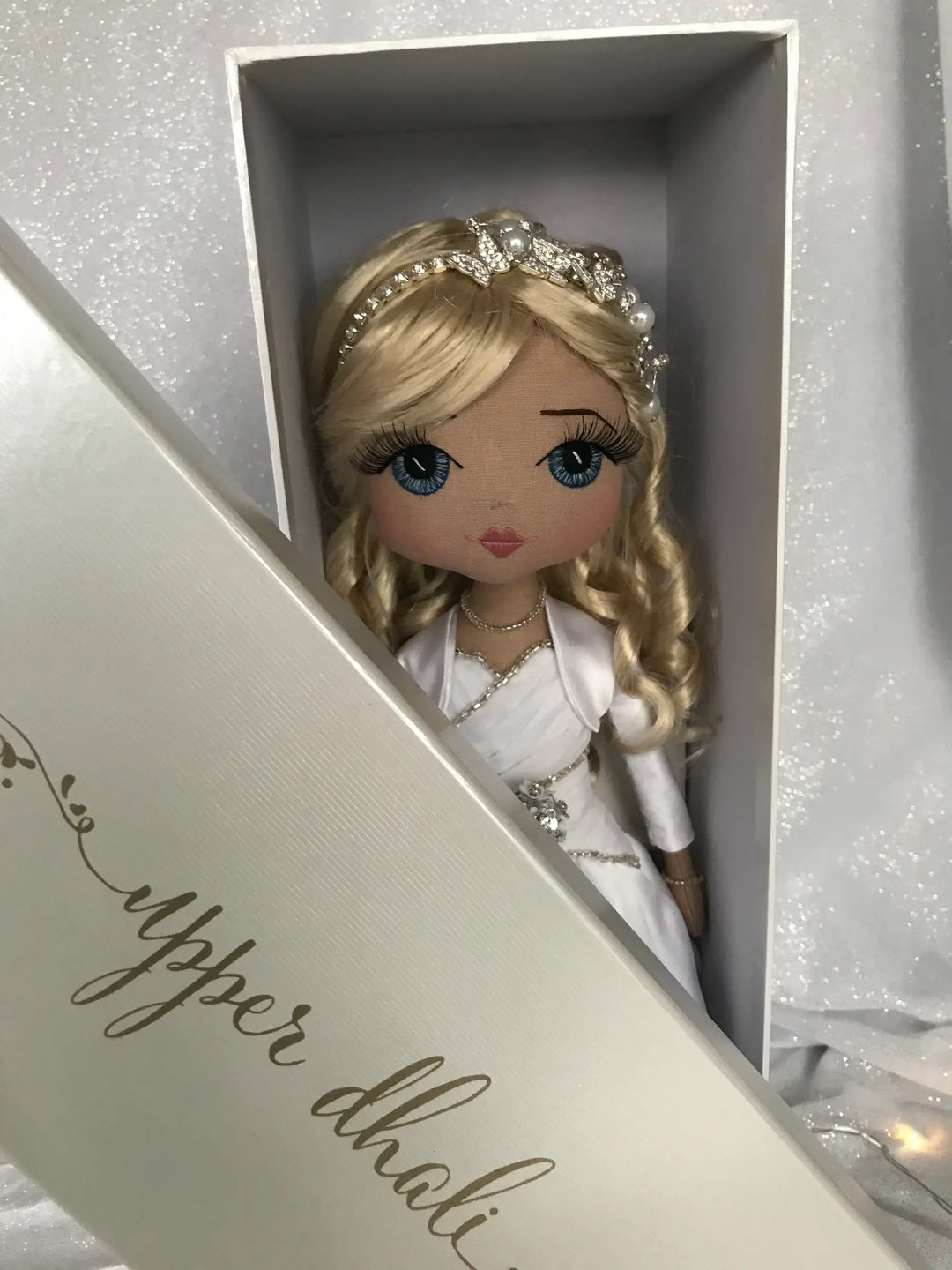 Doll in a white dress with a tiara peeking out of a decorative box.