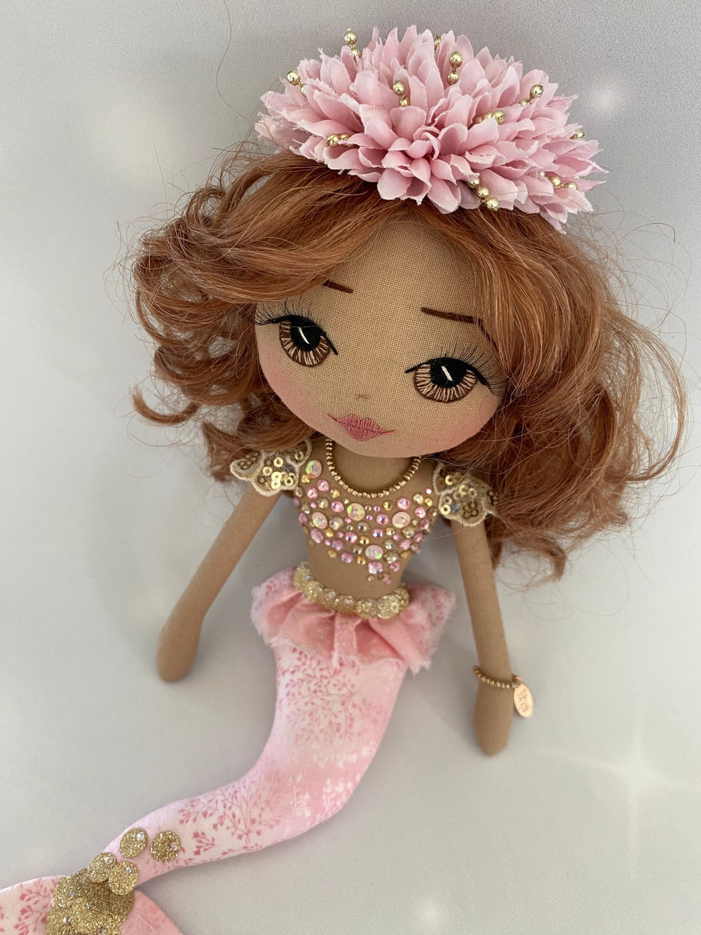 Doll with pink and gold outfit and floral headpiece on a white background