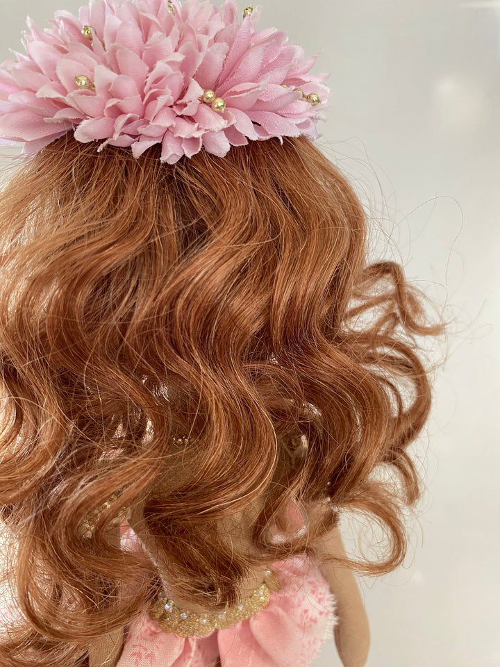 Close-up of a person with wavy brown hair wearing a pink floral headband against a white background