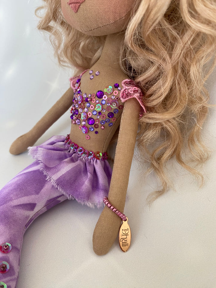 Doll with blonde hair, purple outfit, and sequined top on a light background