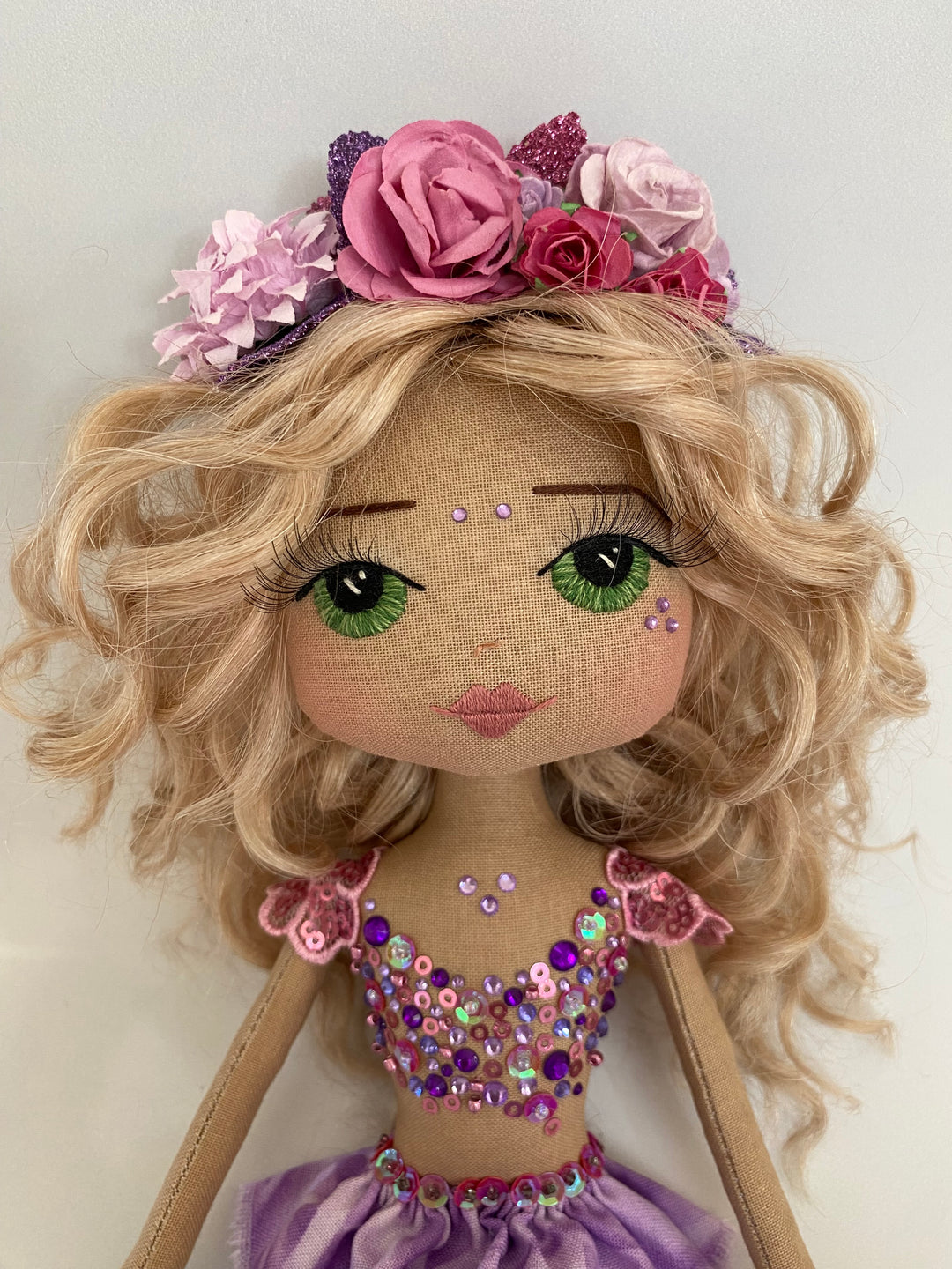 Textile doll with blonde hair, floral headband, and colorful embellishments on a white background