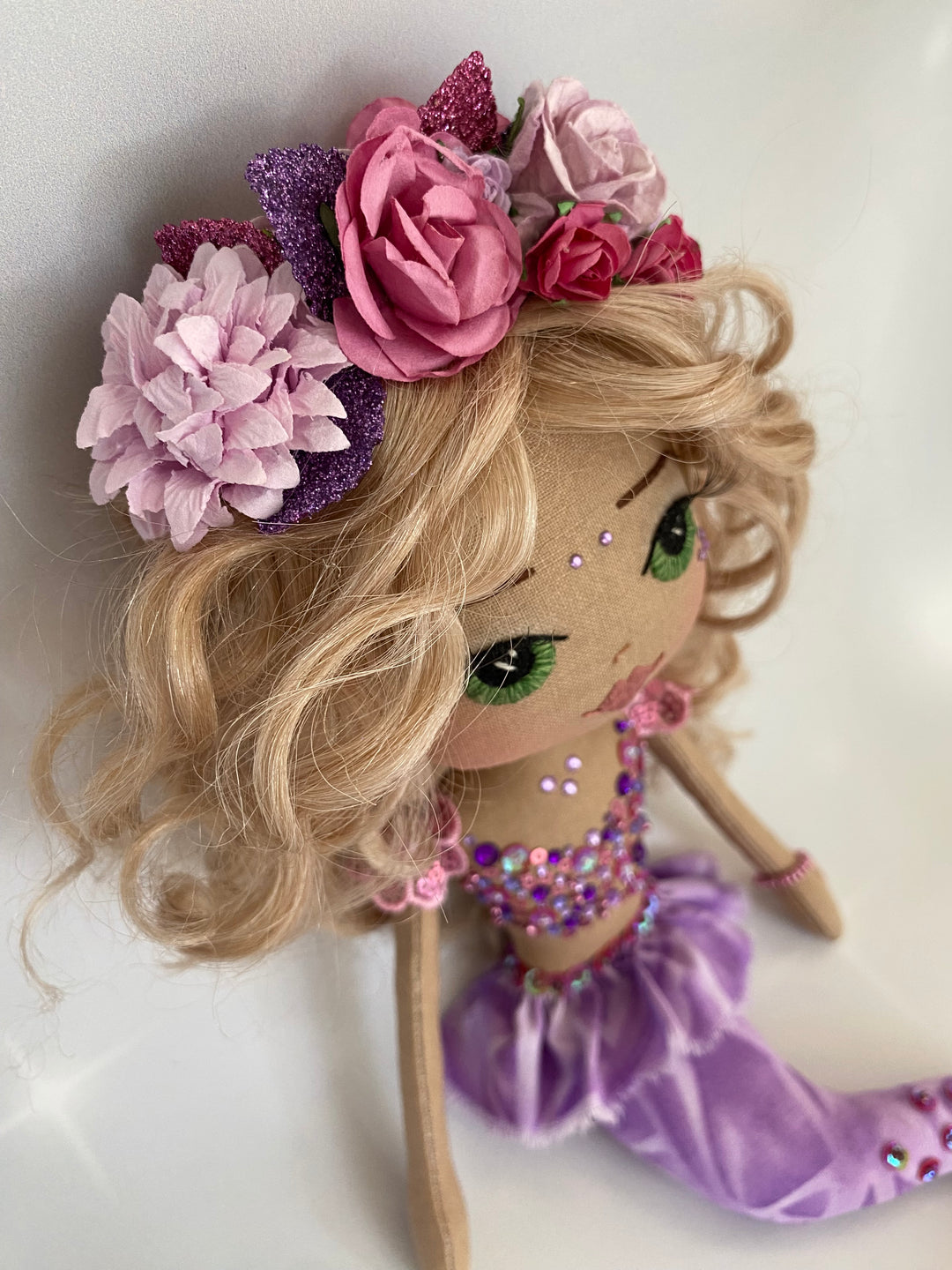 Mermaid art doll with blonde hair, flowers, and a purple bow on a white background