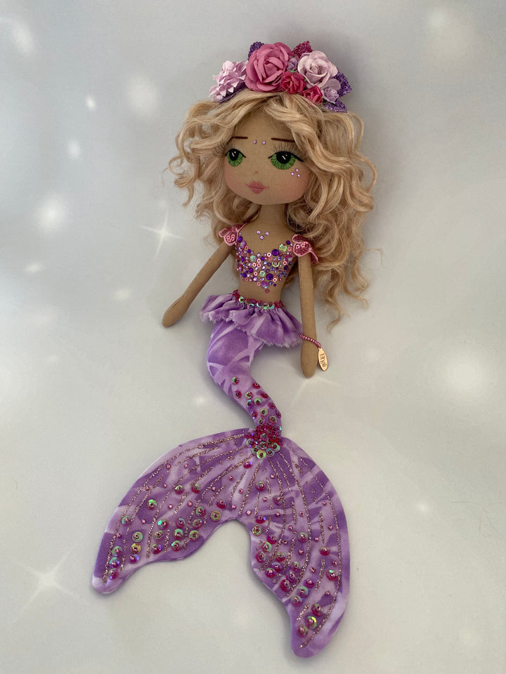 Handmade mermaid doll with purple tail and pink detail, she has long sandy blond curly hair with hand embroidered green eyes and a pink and purple flower mermaid crown