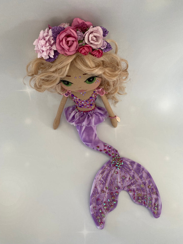 Mermaid toy with blonde hair, pink flowers, and a purple tail on a white background