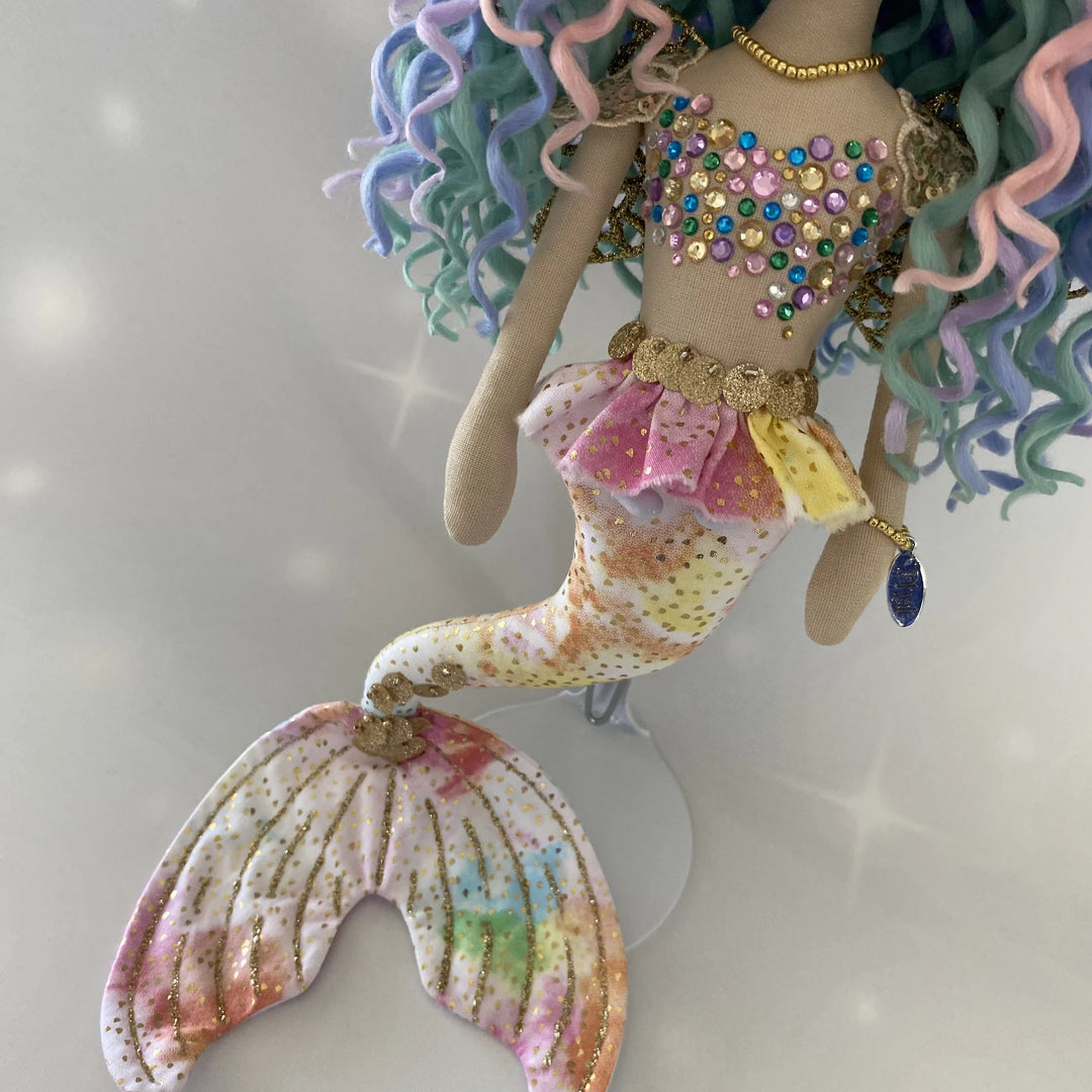 Side-angle view of the Kalani Auralis rainbow mermaid doll, highlighting her pastel tail, golden accents and detailed beaded bodice.