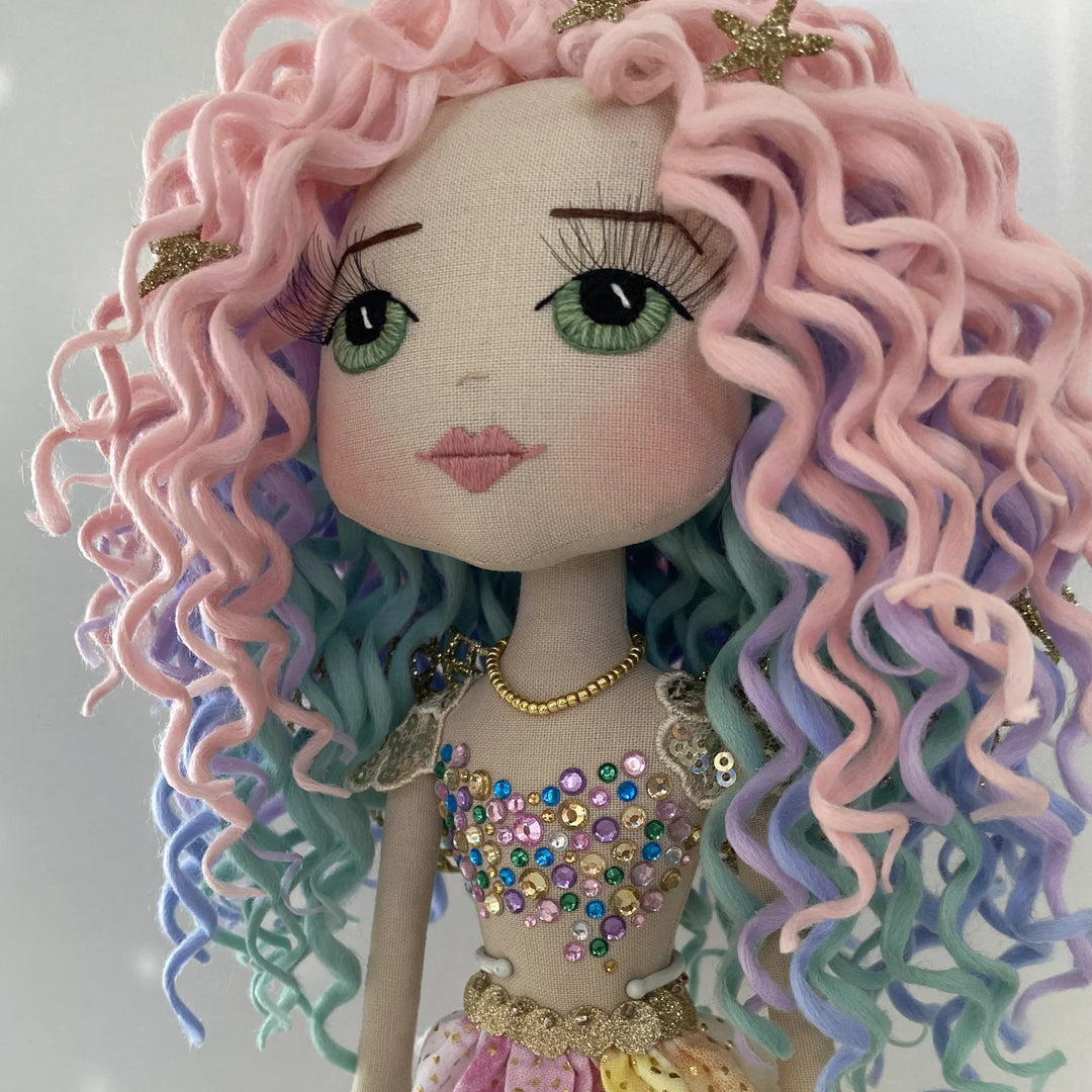 Front view of Kalani Auralis’ pastel rainbow curls, showing pink, lilac, aqua and blue tones crowned with glittery gold starfish.