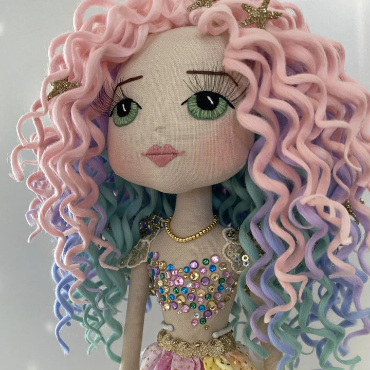 Front view of Kalani Auralis’ pastel rainbow curls, showing pink, lilac, aqua and blue tones crowned with glittery gold starfish.