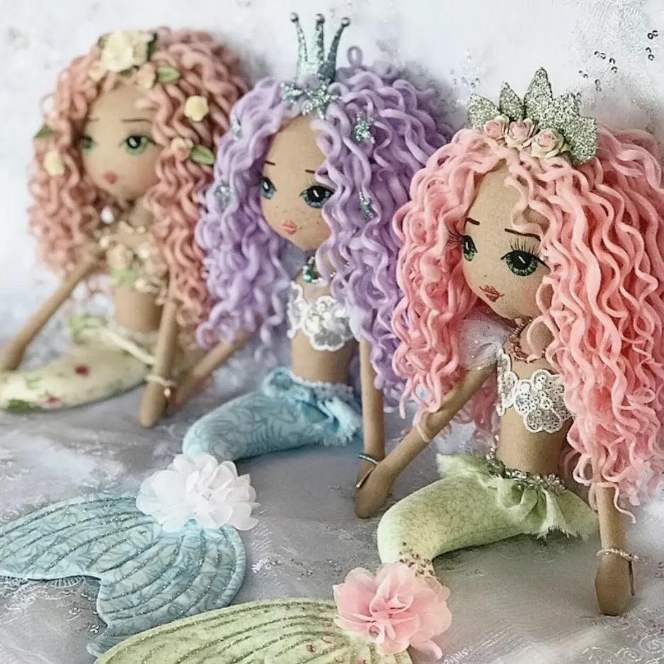 Three mermaid dolls with pastel hair and tails on a light background