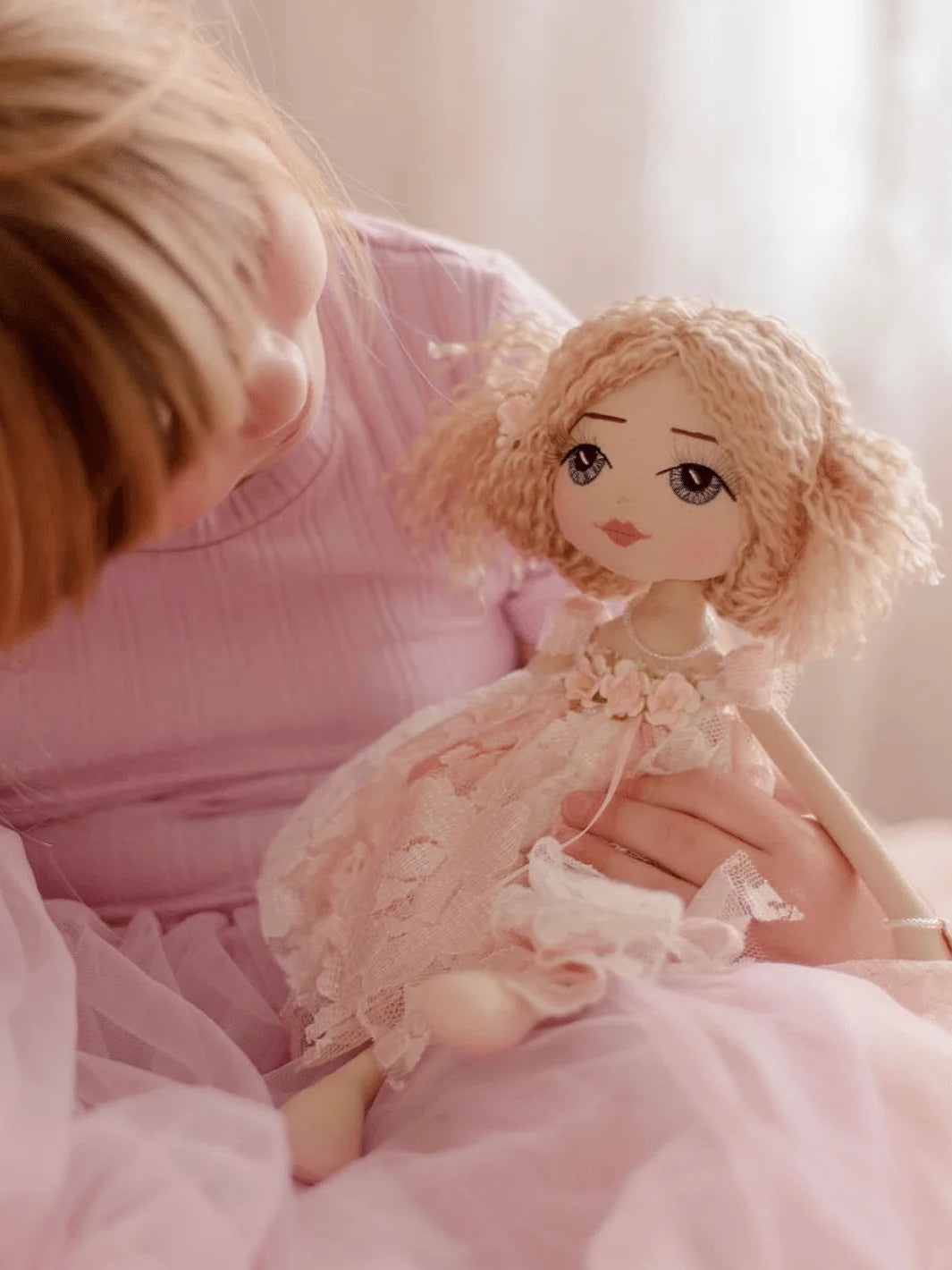 Handmade doll with blue eyes and blonde hair being held by a young girl wearing lavender dress