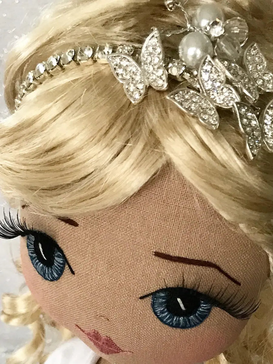 Fabric doll with blonde hair and blue eyes wearing a decorative headband.