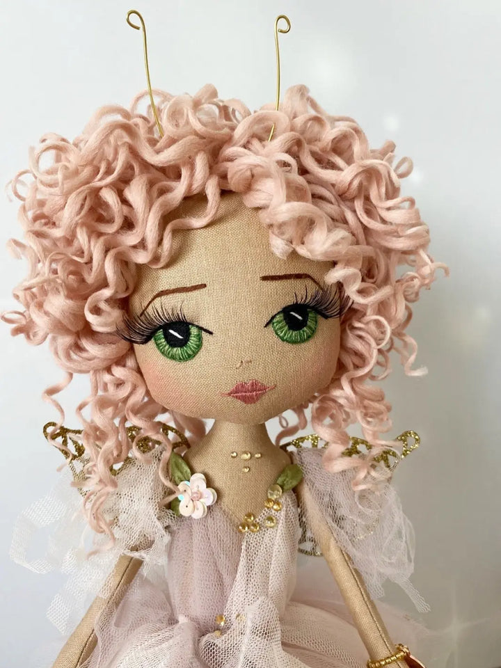Pink handmade fairy doll with embroidered face. Featuring gold fairy wings, green eyes, pink hand rolled curly hair