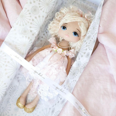 handmade doll wearing a pink and white lace dress with three flowers & ribbon on the bodice. She has short blonde sequin hair, hand embroidered blue eyes and eyelashes.