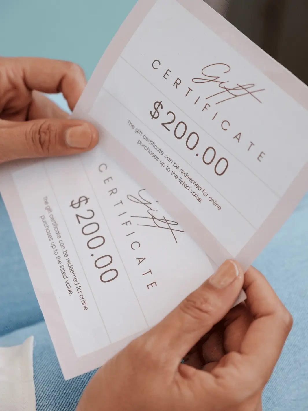 Two $200 gift certificates held by hands against a light blue background
