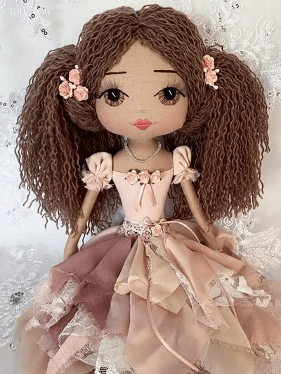 handmade doll with hand embroidered brown eyes, long brown hair in ponytails with flower detail, wearing a vintage inspired chiffon and lace dress in pink tones with flower and ribbon detail